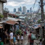 狭い路地に密集する住宅地の奥に近代的な高層ビル群が見える都市景観。スラムと現代都市の格差を象徴している